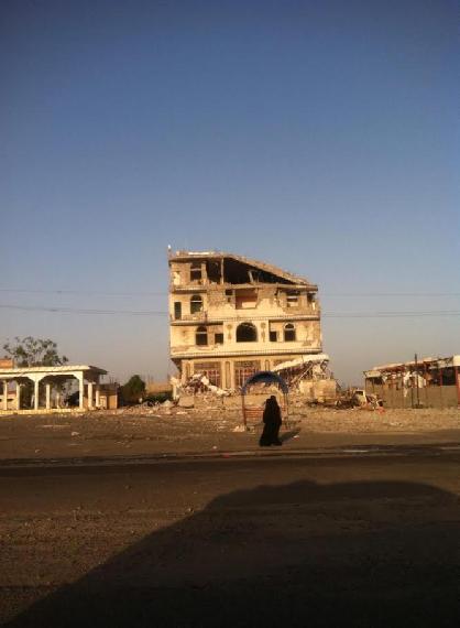 A woman standing in front of her damaged house in Aden